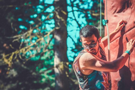 Man on climbing wall at Camp Wildfire. A summer weekend break in a forest near London and Kent. An outdoor woodland retreat featuring adventure activities, live music, DJs, parties and camping. Half summer adventure activity camp, half music festival, for adults only.