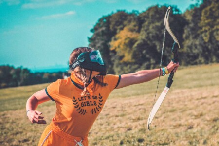 Girl with bow and arrow at archery at Camp Wildfire. A summer weekend break in a forest near London and Kent. An outdoor woodland retreat featuring adventure activities, live music, DJs, parties and camping. Half summer adventure activity camp, half music festival, for adults only.