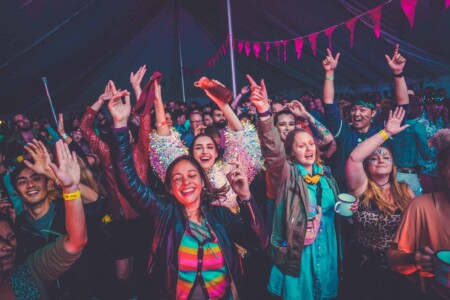 Crowd having fun in the discotheque tent at Camp Wildfire. A summer weekend break in a forest near London and Kent. An outdoor woodland retreat featuring adventure activities, live music, DJs, parties and camping. Half summer adventure activity camp, half music festival, for adults only.