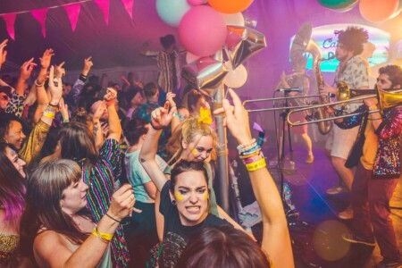 The crowd dancing to the band in the discotheque tent at Camp Wildfire. A summer weekend break in a forest near London and Kent. An outdoor woodland retreat featuring adventure activities, live music, DJs, parties and camping. Half summer adventure activity camp, half music festival, for adults only.