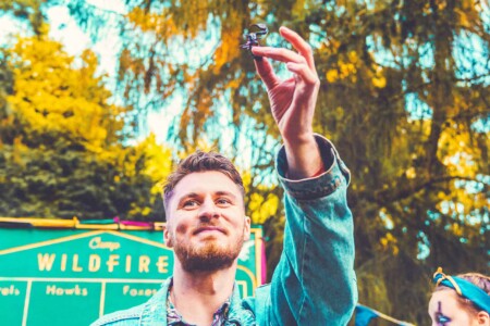 Guy in denim jacket taking part in the bushtucker trial at Camp Wildfire. A summer weekend break in a forest near London and Kent. An outdoor woodland retreat featuring adventure activities, live music, DJs, parties and camping. Half summer adventure activity camp, half music festival, for adults only.