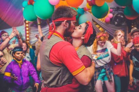 Couple having a romantic kiss whilst partying at Camp Wildfire. The UK's Best Alternative Festival. UK's Top Unique Event. A summer weekend break in a forest near London and Kent. An outdoor woodland retreat featuring adventure activities, live music, DJs, parties and camping. Half summer adventure activity camp, half music festival, for adults only.