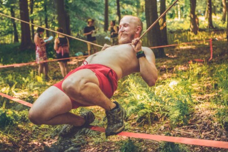 Man balancing on cords at the puzzle activity at Camp Wildfire. A summer weekend break in a forest near London and Kent. An outdoor woodland retreat featuring adventure activities, live music, DJs, parties and camping. Half summer adventure activity camp, half music festival, for adults only.