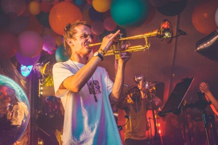 Guy playing trumpet in the discotheque tent at Camp Wildfire. A summer weekend break in a forest near London and Kent. An outdoor woodland retreat featuring adventure activities, live music, DJs, parties and camping. Half summer adventure activity camp, half music festival, for adults only.