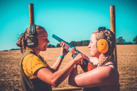 Girl learning how to shoot clay pigeons at Camp Wildfire. A summer weekend break in a forest near London and Kent. An outdoor woodland retreat featuring adventure activities, live music, DJs, parties and camping. Half summer adventure activity camp, half music festival, for adults only.