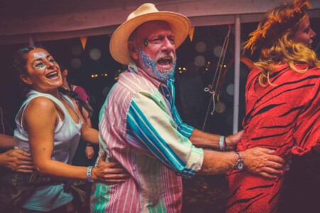 Man with a glittery beard doing the conga in the discotheque tent at Camp Wildfire. A summer weekend break in a forest near London and Kent. An outdoor woodland retreat featuring adventure activities, live music, DJs, parties and camping. Half summer adventure activity camp, half music festival, for adults only.