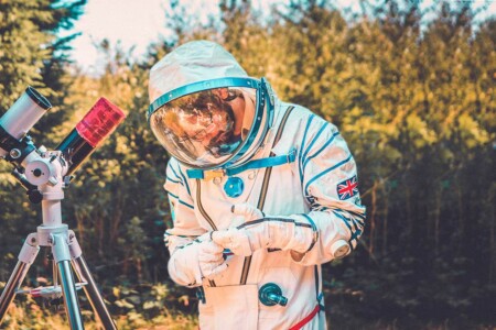 Man dressed as an astronaut with a telescope at the space science activity at Camp Wildfire. A summer weekend break in a forest near London and Kent. An outdoor woodland retreat featuring adventure activities, live music, DJs, parties and camping. Half summer adventure activity camp, half music festival, for adults only.