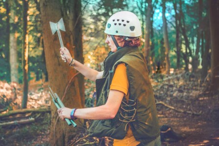 Girl participating in the axe throwing activity at Camp Wildfire. A summer weekend break in a forest near London and Kent. An outdoor woodland retreat featuring adventure activities, live music, DJs, parties and camping. Half summer adventure activity camp, half music festival, for adults only.