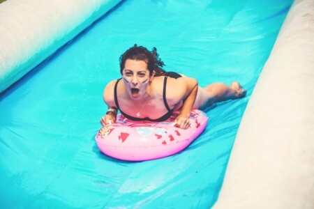 Girl flying down the waterslide at Camp Wildfire. Group of people wearing tie dye joining in a group session of yoga outside at Camp Wildfire. The UK's Best Alternative Festival. UK's Top Unique Event. A summer weekend break in a forest near London and Kent. An outdoor woodland retreat featuring adventure activities, live music, DJs, parties and camping. Half summer adventure activity camp, half music festival, for adults only.