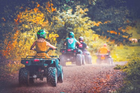 Girl in yellow dress wearing a helmet quad biking at Camp Bestival. The UK's Best Alternative Festival. UK's Top Unique Event. A summer weekend break in a forest near London and Kent. An outdoor woodland retreat featuring adventure activities, live music, DJs, parties and camping. Half summer adventure activity camp, half music festival, for adults only.