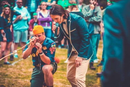 Person in patrol uniform with badges on playing a patrol game at Camp Wildfire. A summer weekend break in a forest near London and Kent. An outdoor woodland retreat featuring adventure activities, live music, DJs, parties and camping. Half summer adventure activity camp, half music festival, for adults only.