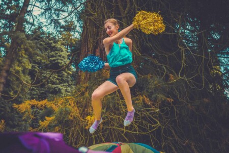 Girl trampolining whilst cheerleading with pom poms at Camp Wildfire. The UK's Best Alternative Festival. UK's Top Unique Event. A summer weekend break in a forest near London and Kent. An outdoor woodland retreat featuring adventure activities, live music, DJs, parties and camping. Half summer adventure activity camp, half music festival, for adults only.