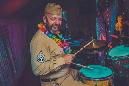 Band member of Company B Swing on the drums at Camp Wildfire. A summer weekend break in a forest near London and Kent. An outdoor woodland retreat featuring adventure activities, live music, DJs, parties and camping. Half summer adventure activity camp, half music festival, for adults only.