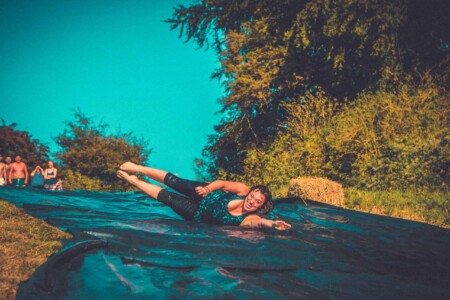 Girl on the extreme water slide. A summer weekend break in a forest near London and Kent. An outdoor woodland retreat featuring adventure activities, live music, DJs, parties and camping. Half summer adventure activity camp, half music festival, for adults only.