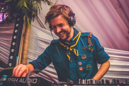 Lee in his patrol uniform on the decks in the discotheque tent at Camp Wildfire. A summer weekend break in a forest near London and Kent. An outdoor woodland retreat featuring adventure activities, live music, DJs, parties and camping. Half summer adventure activity camp, half music festival, for adults only.