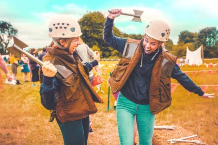 Two girls at the axe throwing activity at Camp Wildfire. A summer weekend break in a forest near London and Kent. An outdoor woodland retreat featuring adventure activities, live music, DJs, parties and camping. Half summer adventure activity camp, half music festival, for adults only.