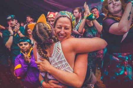 A couple of adventurers having a hug on the dance floor at the discotheque at Camp Wildfire. A summer weekend break in a forest near London and Kent. An outdoor woodland retreat featuring adventure activities, live music, DJs, parties and camping. Half summer adventure activity camp, half music festival, for adults only.