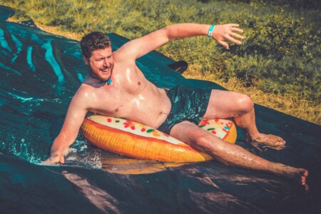 Man on extreme water slide at Camp Wildfire. A summer weekend break in a forest near London and Kent. An outdoor woodland retreat featuring adventure activities, live music, DJs, parties and camping. Half summer adventure activity camp, half music festival, for adults only.