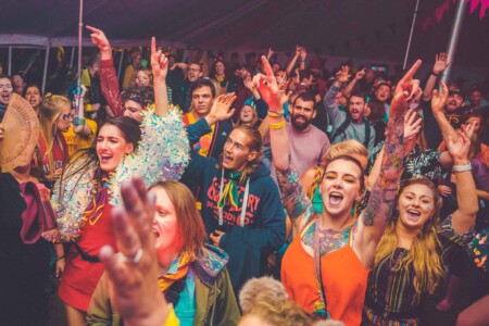 The crowd with there hands up in the discotheque tent at Camp Wildfire. A summer weekend break in a forest near London and Kent. An outdoor woodland retreat featuring adventure activities, live music, DJs, parties and camping. Half summer adventure activity camp, half music festival, for adults only.