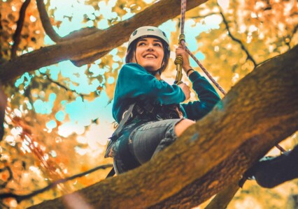 Girl wearing helmet climbing trees at Camp Wildfire. The UK's Best Alternative Festival. UK's Top Unique Event. A summer weekend break in a forest near London and Kent. An outdoor woodland retreat featuring adventure activities, live music, DJs, parties and camping. Half summer adventure activity camp, half music festival, for adults only.