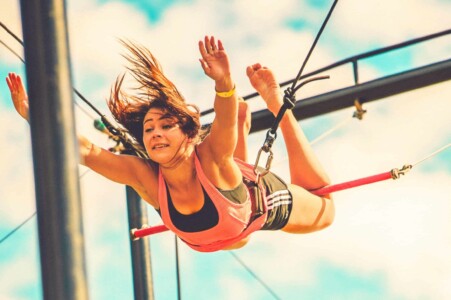 Girl flying in the air on the trapeze at Camp Wildfire. The UK's Best Alternative Festival. UK's Top Unique Event. A summer weekend break in a forest near London and Kent. An outdoor woodland retreat featuring adventure activities, live music, DJs, parties and camping. Half summer adventure activity camp, half music festival, for adults only.